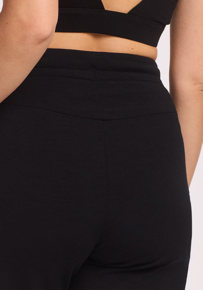 A close-up of a person wearing a black sports bra and Woolx Willa Joggers - Black, highlighting their back and waist.