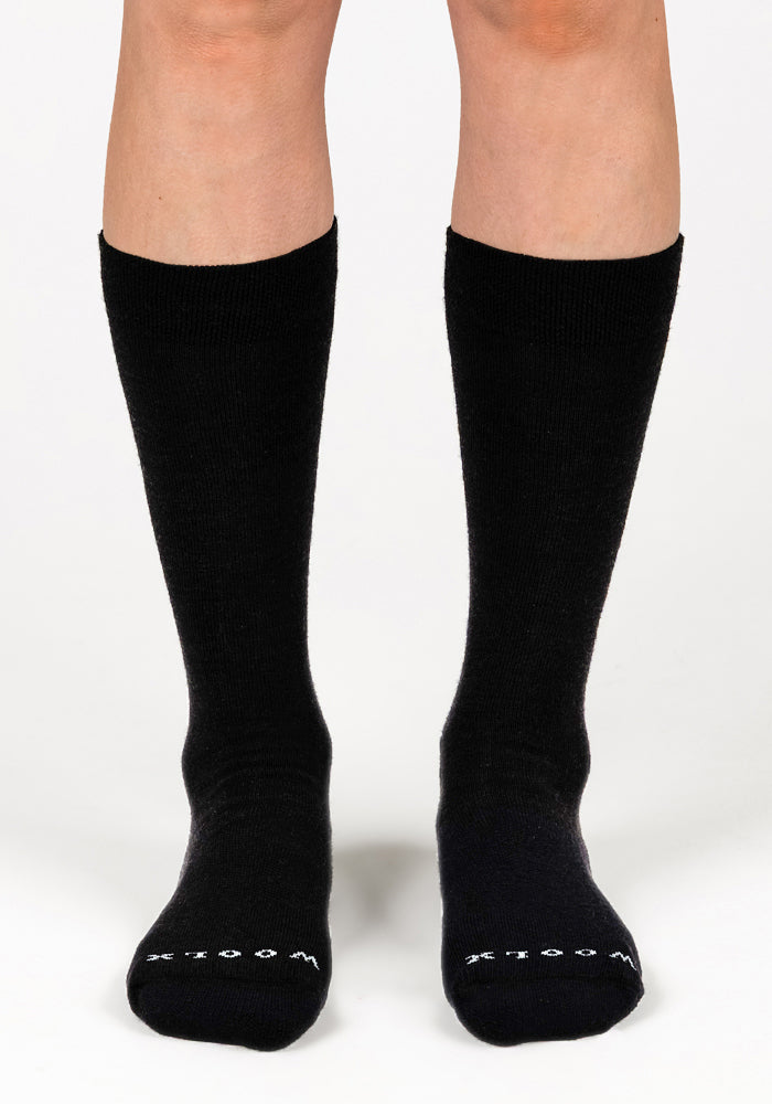 A person wearing black Woolx Womens Chandler Mid Calf Socks stands on a white background. The word "WOODS" appears in white letters on the toes of both odor-resistant socks.