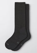 The Woolx Womens Chandler Mid Calf Sock in black is pictured laid flat on a light gray background, with one sock overlapping the other. It features a simple, minimal design and subtle toe text.