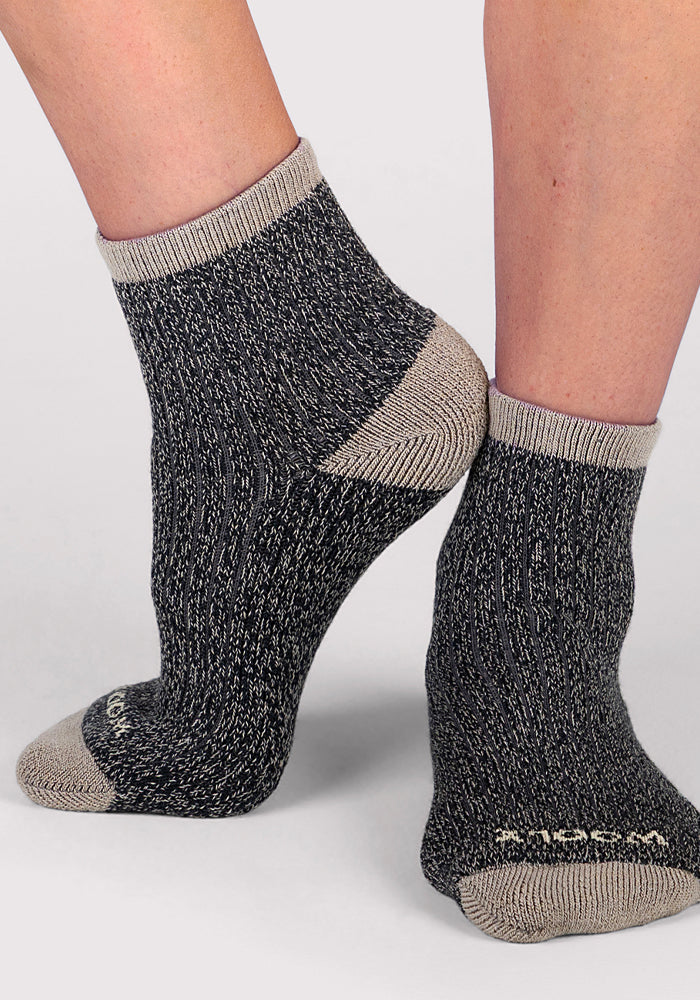 A close-up of two feet wearing Woolx Womens Cozy Mini Crew Socks in black and gray with light gray cuffs, heels, and toes, set against a plain light background.