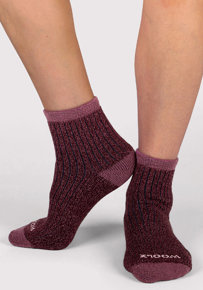 A woman models Woolx Womens Cozy Mini Crew Socks—dark red with ribbed texture and light purple cuffs, heels, and toes—standing with one foot slightly ahead on a light background.