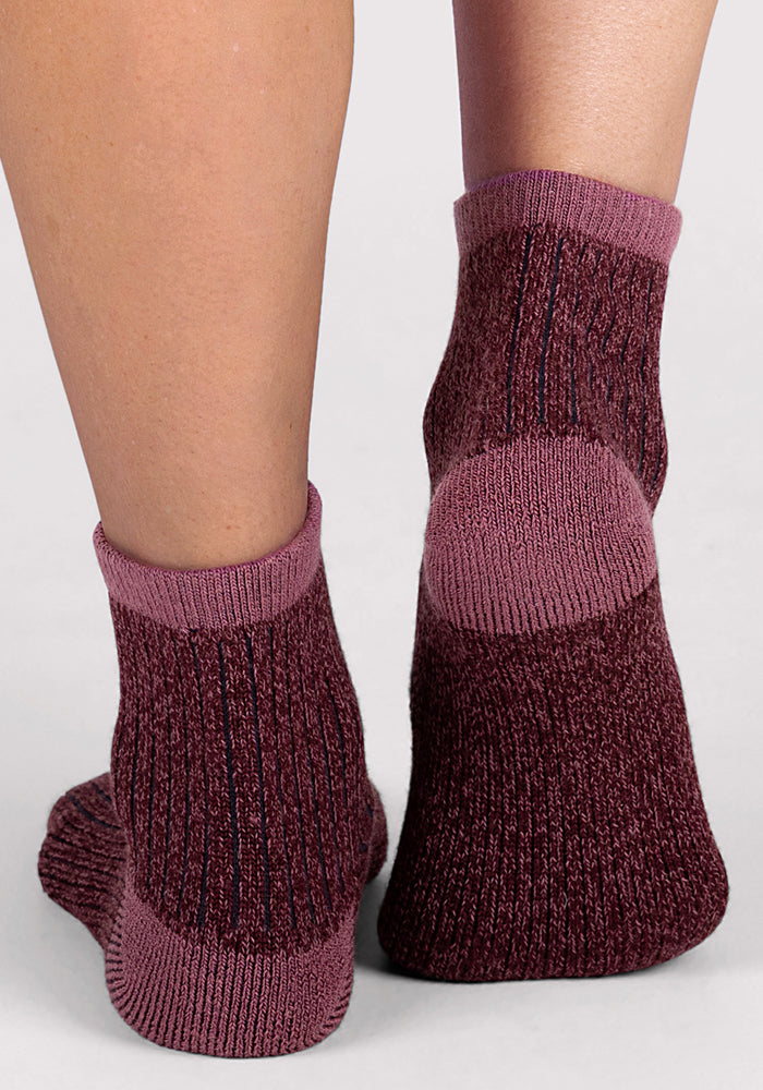 A close-up view of two feet wearing Woolx Womens Cozy Mini Crew Socks in maroon and purple ribbed Merino wool, standing on a light gray surface.