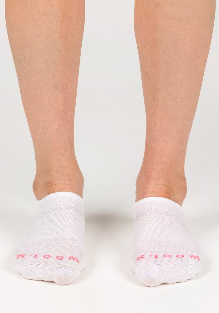 Someone stands on a white surface wearing Woolx Womens Daisy Ped Socks - White Lightning, featuring pink "WOOLX" lettering on the toes.