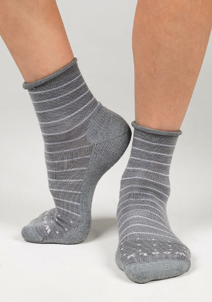 Two feet in Woolx Womens Derby Roll Top Socks - Grey, featuring thin white stripes, stand on a light surface—one flat, the other raised on its toes—highlighting the breathable design.
