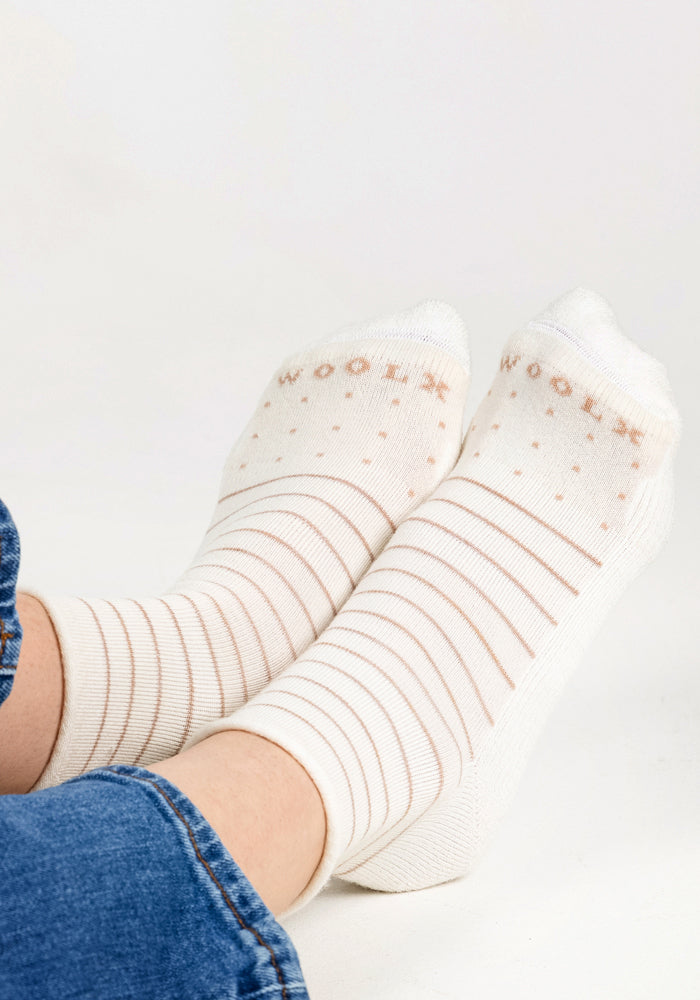 Close-up of a person’s feet in Woolx Womens Derby Roll Top Sock - Sand Dollar, featuring light beige polka dots and stripes, paired with blue jeans against a plain white background.
