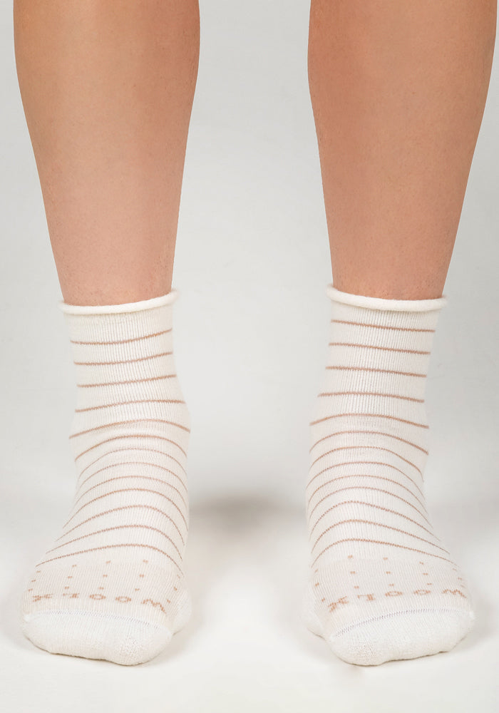 A pair of feet models the Woolx Womens Derby Roll Top Sock in Sand Dollar—a stylish, breathable sock featuring thin beige stripes and a comfy roll top, shown on a light-colored surface.
