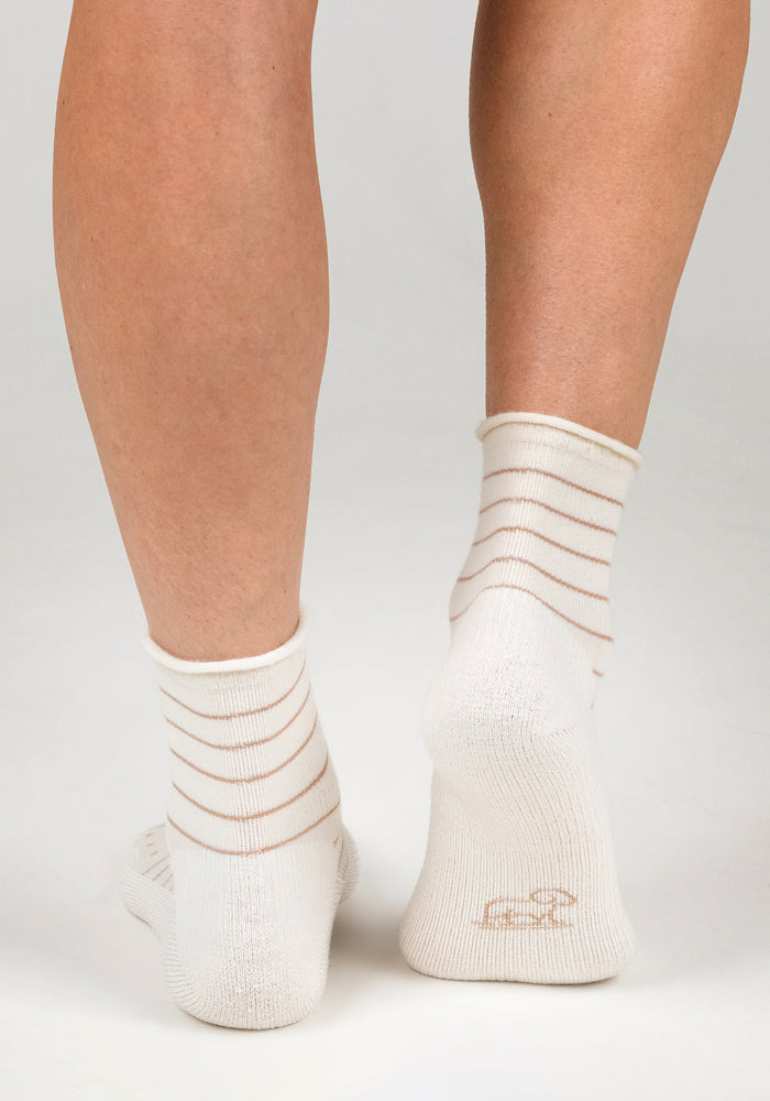 A close-up of two feet from behind wearing Woolx Womens Derby Roll Top Socks in Sand Dollar—white socks with thin beige stripes—against a plain light background.