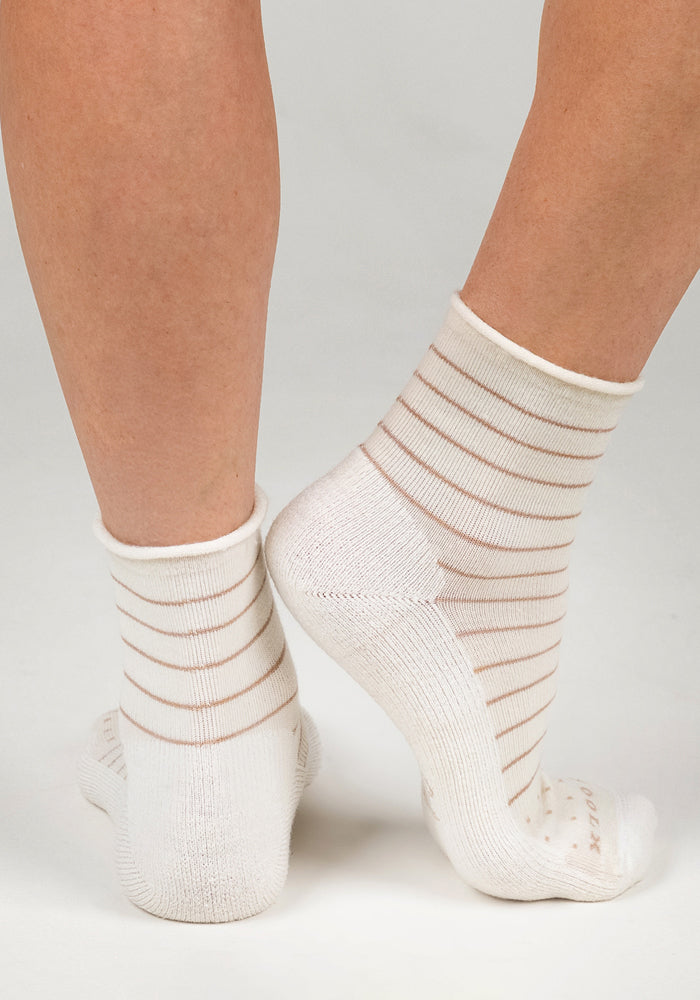 A close-up of two feet in Woolx Womens Derby Roll Top Sock - Sand Dollar, featuring white breathable fabric with thin beige stripes, standing on a plain light background with heels together and toes pointing outward.
