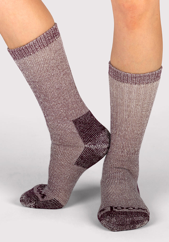 Two feet in Woolx Womens Extreme Crew Socks—Windsor Wine, one flat and one on its toes, stand out against a plain backdrop, highlighting cozy merino wool socks perfect for women's cold weather comfort.