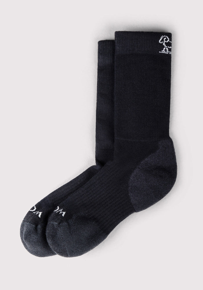 The Woolx Womens Harbor Crew Sock in black features slightly darker heels and toes plus a small white embroidered detail near the top. These moisture-wicking Merino wool crew socks are displayed neatly on a light gray background.
