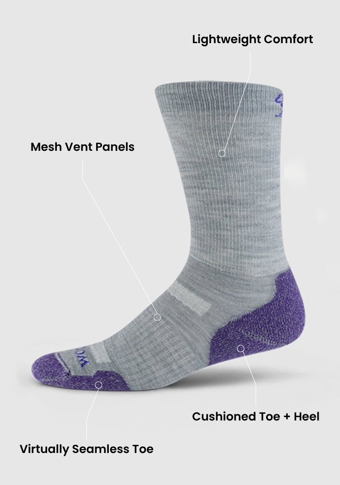 The Woolx Womens Harbor Crew Sock Light Cushion in black features lightweight comfort, mesh vent panels, a virtually seamless toe, and cushioned toe and heel. The sock is showcased elevated against a plain gray background.