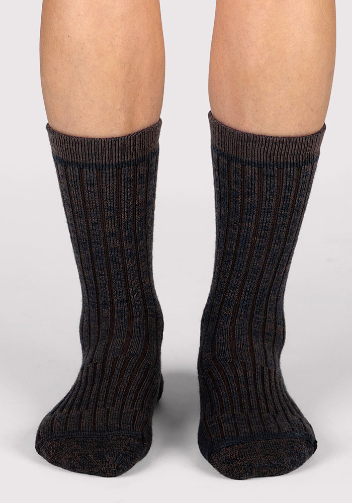 A close-up of a person wearing Woolx Womens Joey Crew Socks in a dark, ribbed design, standing with both feet forward on a light surface.
