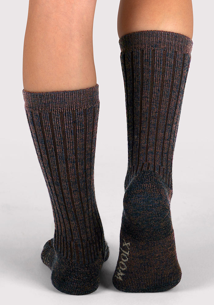 A close-up shows two feet wearing Woolx Womens Joey Mid Calf Socks in Dark Espresso, with ribbed texture, muted colors, and "SOCKS" on the right heel against a light gray background.