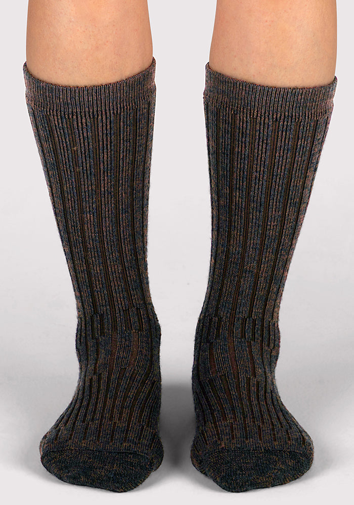 A pair of feet wear Woolx Womens Joey Mid Calf Socks in Dark Espresso—thick, ribbed merino wool socks reaching mid-calf—shown standing on a light, neutral background.