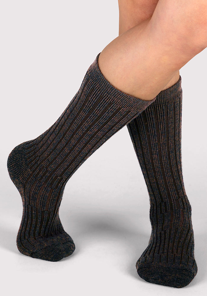 A person with light skin is wearing Woolx Womens Joey Mid Calf Socks in Dark Espresso, standing with one leg crossed over the other against a plain light background.