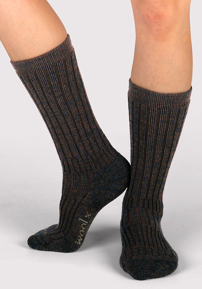 A person wears Woolx Womens Joey Mid Calf Socks in Dark Espresso, standing on a light gray background with one foot slightly raised and the other flat.