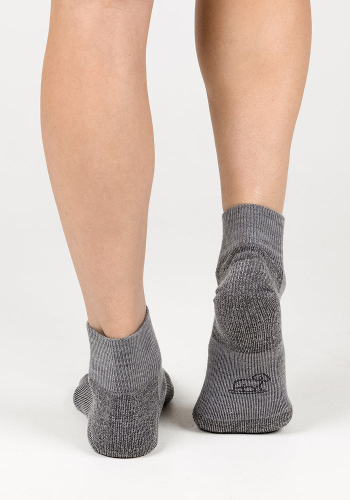 A woman wearing Woolx Womens Rambler Ankle Sock in Pebble stands with feet slightly apart, photographed from behind on a white background, highlighting comfort and moisture management.