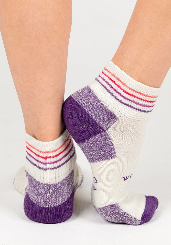 Two feet in Woolx Womens Rambler Ankle Sock - Sand Dollar, featuring white with purple heels and toes plus pink and red ankle stripes, stand heel to heel—ideal for comfort and moisture management with Merino wool.