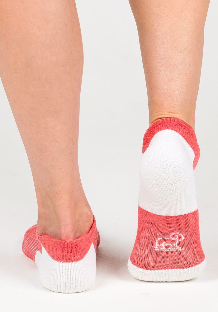 A close-up of two feet in Woolx Womens Rowan No Show Socks - Taffy Twist. One foot is flat, displaying a white logo on the sole, while the other is slightly lifted, showing the pink and white back of the sock.
