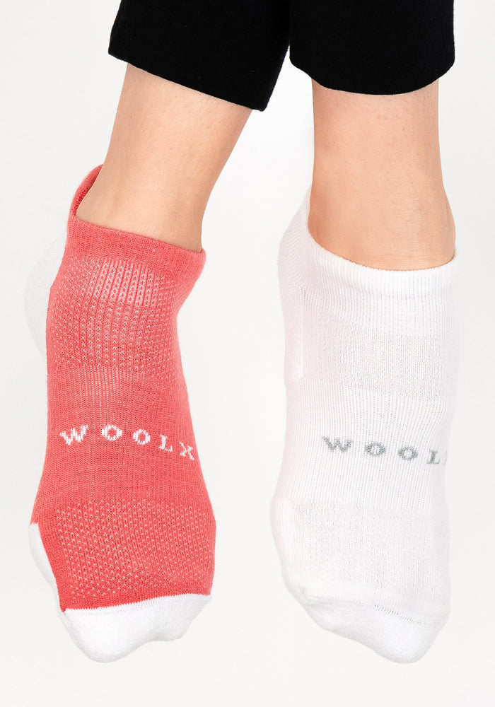 A person wearing mismatched Womens Rowan No Show Socks—one in red, one in White Lightning, both by Woolx—stands against a plain white background.