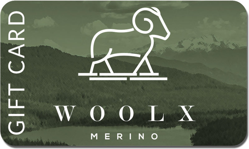 The Woolx Gift Card showcases a minimalist design of a ram on a hill with "WOOLX" and "MERINO" beneath, all set against a scenic mountain backdrop. The card is primarily green and adorned with clouds.